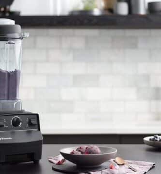 Licuadora vitamix 5200 sobre una mesa negra de una cocina moderna. Dentro del vaso de la licuadora se observa una bebida de color violeta. A sus cotados se ven ingredientes frescos como aguacate u arándanos.