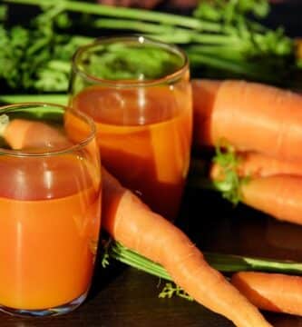 zanahorias recien cortadas con dos vasos de vidrio con jugo de zanahoria y apio