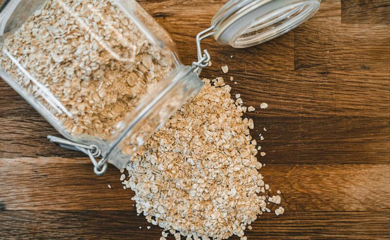 Frasco con avena derramada en una mesa de madera.